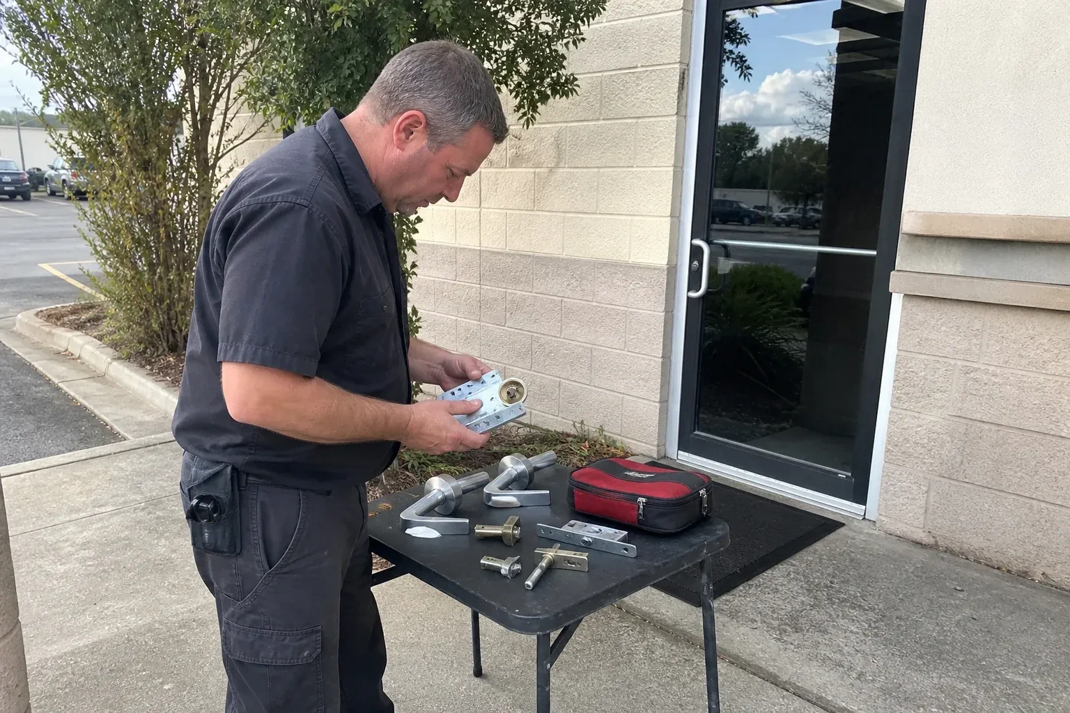 Technician examining detached commercial lock hardware on a table outside a shop entrance. — Business Lockout Service, Uxbridge