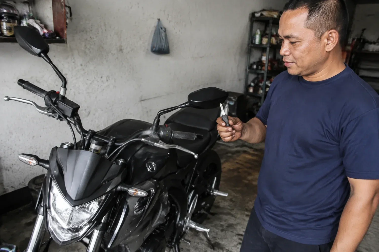 Person holding a key beside a black motorcycle in a garage. — Motorcycle & Scooter Keys, Uxbridge
